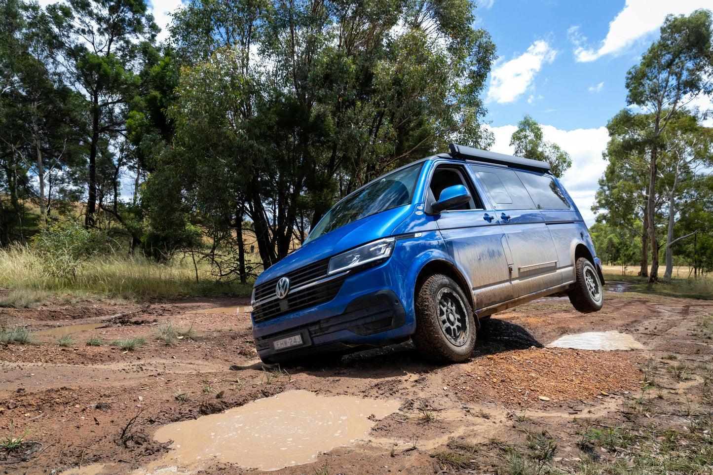 A blue Volkswagen van navigating rough terrain with one wheel airborne