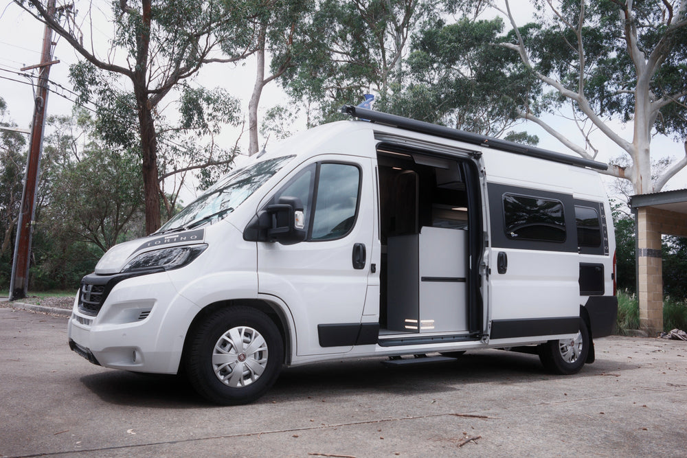 White camper van with open side door parked outdoors near trees