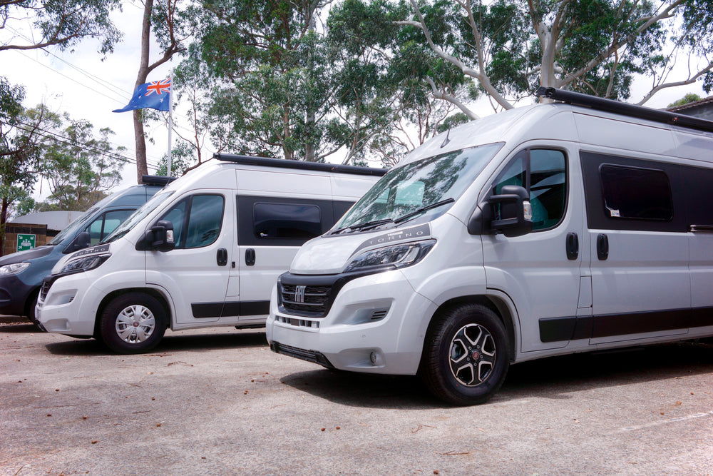 Three white vans parked outdoors with trees in the background and an Australian flag visible