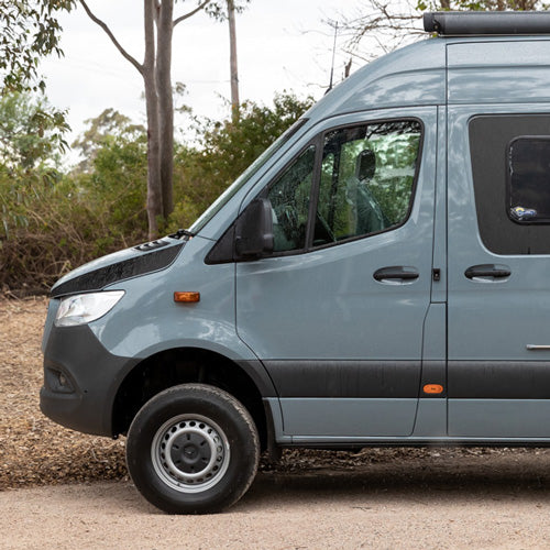 A grey van parked on a dusty road with trees in the background