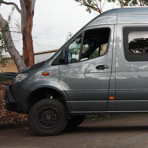 A gray van parked on a street beside trees