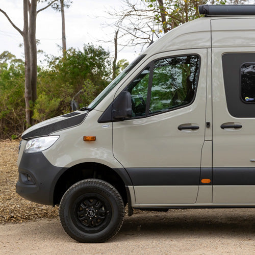 A beige van parked on a gravel surface with trees in the background