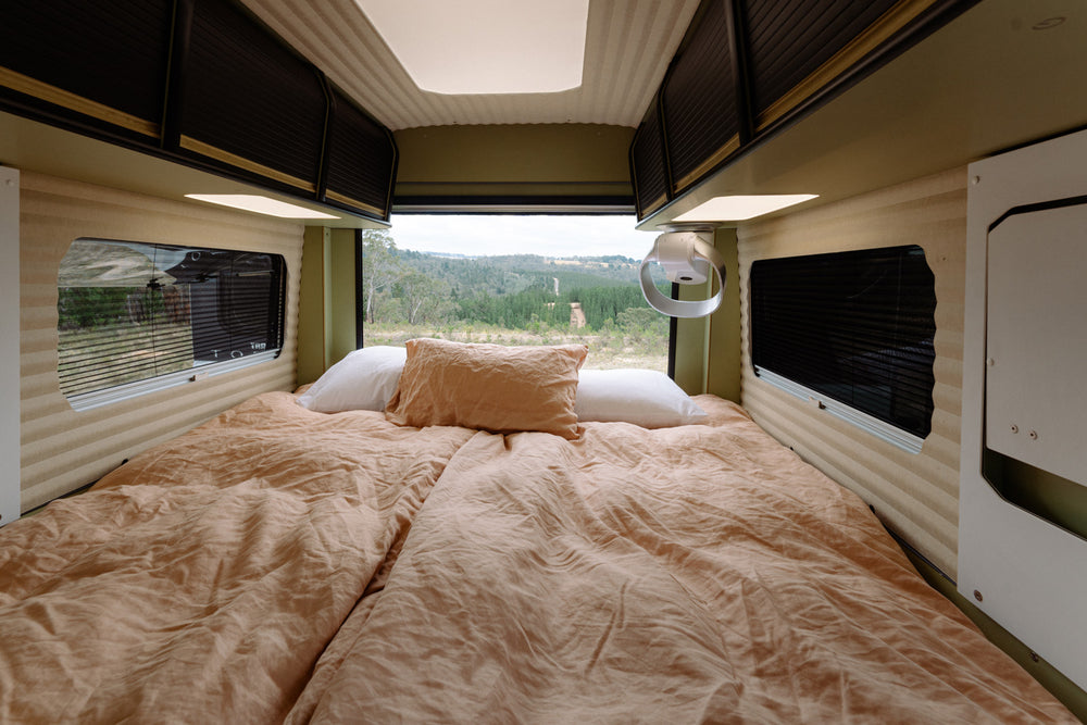 Interior of a camper van with a bed and windows showing a natural landscape outside