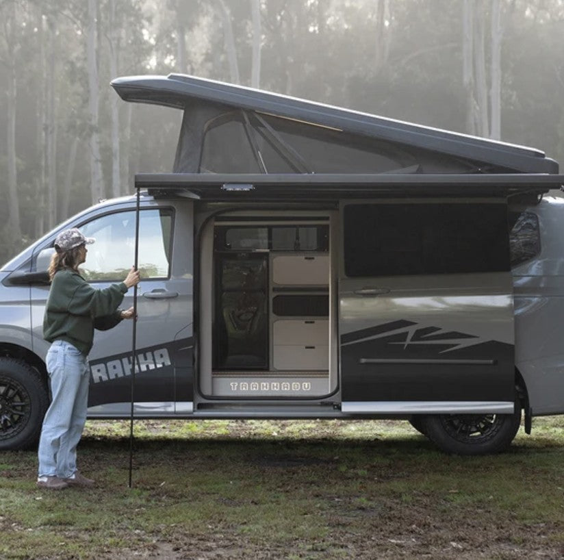 Trakkadu on the Ford Transit Custom with pop top raised, awning out and sliding door open in a misty forest